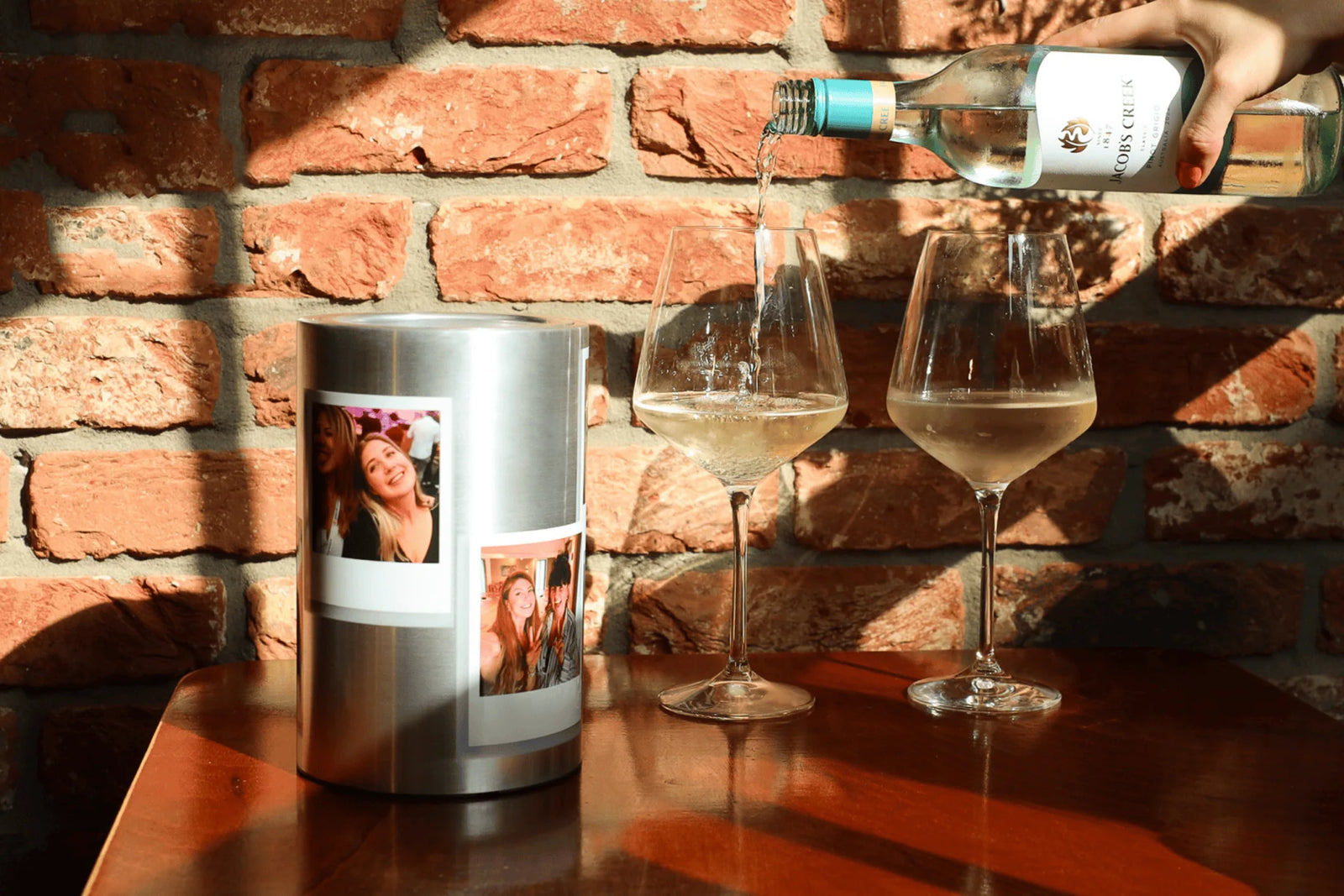 Coolenator polaroid personalized design wine cooler with a bottle of wine on a wooden table with two wine glasses next to it and someone pooring the wine
