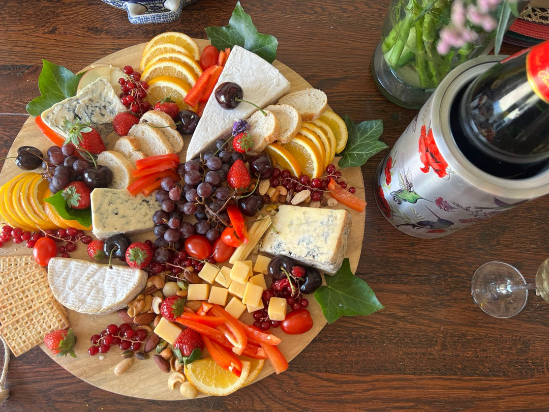 Cheese board with nuts, fruit and different cheeses. Next to it a bottle of white wine in a coolenator wine cooler.