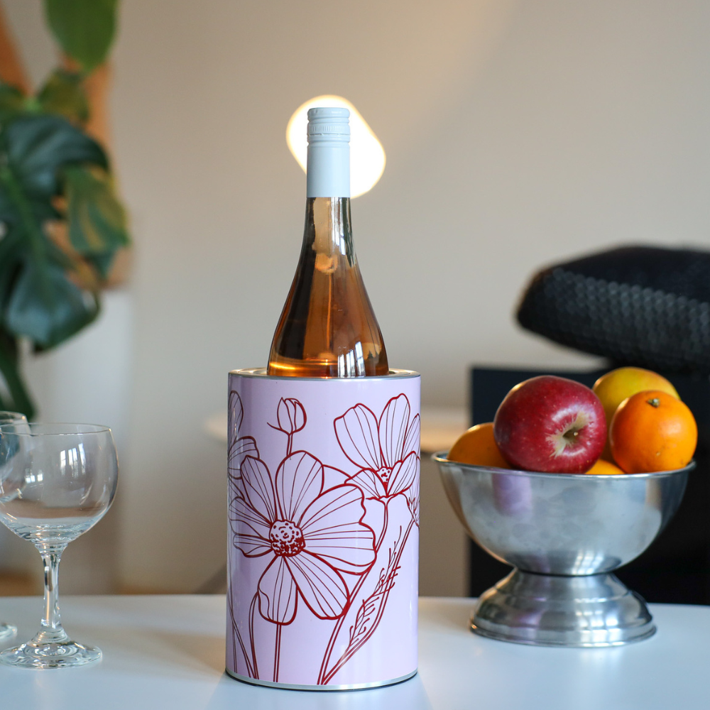 A Coolenator wine cooler on the middle of the white table with a a bottle of rose in it. Wine glasses situated on the left and a bowl of fruit on the right. 